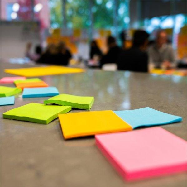 Several pads of colorful sticky notes are scattered on a table. People are in the background.